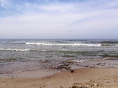 Dalgalar Litvanya 'nın Palanga kentindeki Baltık Denizi' nin kumlu sahillerine çarpar. Gökyüzü parçalı bulutludur, mavi ve beyaz renklerin bir karışımını yaratır. Koyu, ıslak kum ve dağınık kayalar görülebilir.