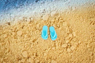 Yaz aylarında deniz yanında kum üzerinde küçük oyuncak mavi flip flop