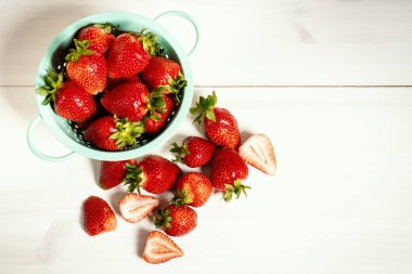 Beyaz ahşap bir masa üzerinde küçük bir kevgir içinde taze kırmızı çilek