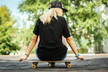 siyah T-shirt kız sırtında bir kaykay üzerinde oturan ve etrafına bakıyor