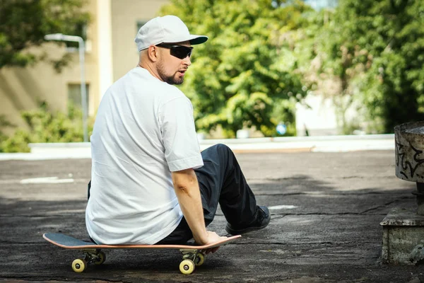 Uomo Una Shirt Bianca Seduto Uno Skateboard Guarda Intorno Una — Foto Stock