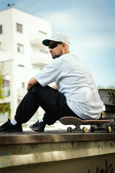 Uomo Una Shirt Bianca Seduto Uno Skateboard Guarda Intorno Una — Foto Stock