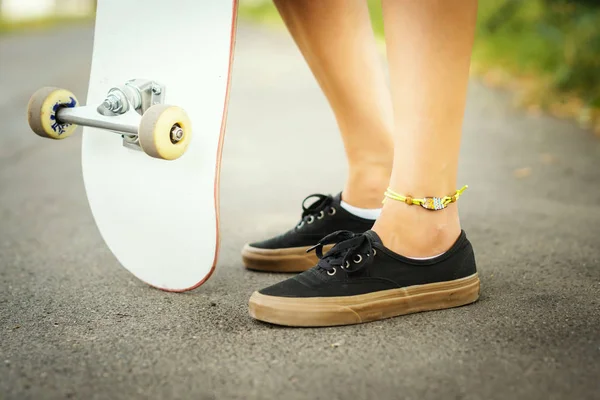 view of the legs of a girl with a skateboard on the street on a summer day