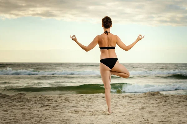 gün batımında sahilde yoga uygulamak bir siyah mayo güzel kadın