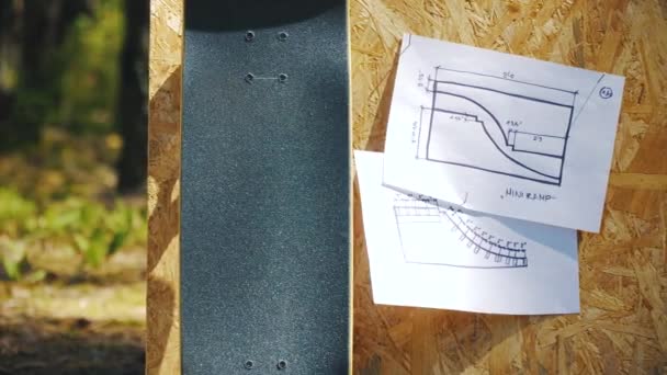 Skateboard on a wooden background with plans for a miniramp in a skatepark — Stock Video