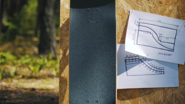 Skateboard on a wooden background with plans for a miniramp in a skatepark — Stock Video