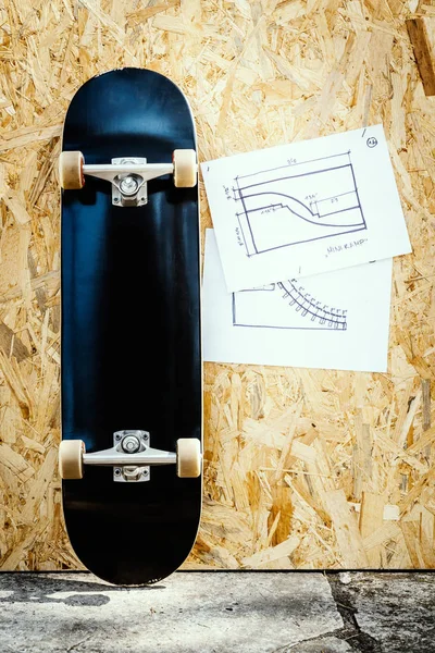 Planche à roulettes sur un fond en bois avec des plans pour un miniramp dans un skatepark — Photo