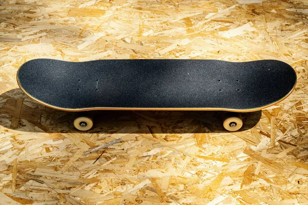 Skateboard with white wheels on a wooden background in a skatepark — Stock Photo, Image