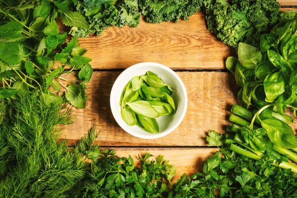 Green vegetables and spices in bowls on a wooden table — Stock Photo, Image