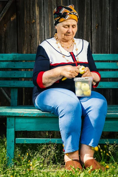 Yaşlı kadın bir bankta oturan ve yeşil elma kesme — Stok fotoğraf