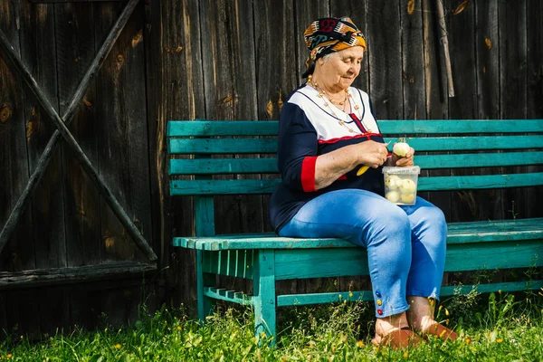 Anciana está sentada en un banco y está cortando manzanas verdes —  Fotos de Stock