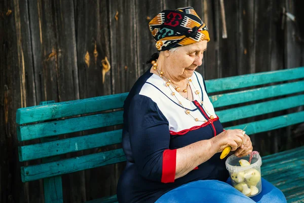 Yaşlı kadın bir bankta oturan ve yeşil elma kesme — Stok fotoğraf