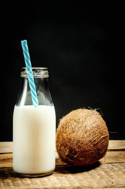 Hindistan cevizi ve şişe süt siyah bir zemin üzerine ahşap bir masa üzerinde