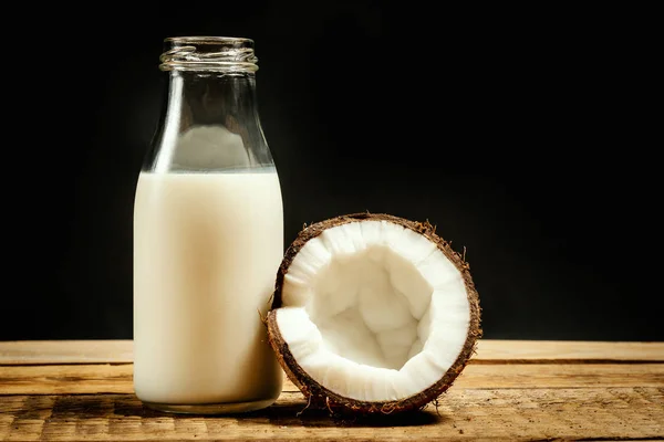 Noci di cocco e bottiglia di latte su un tavolo di legno su sfondo nero — Foto Stock