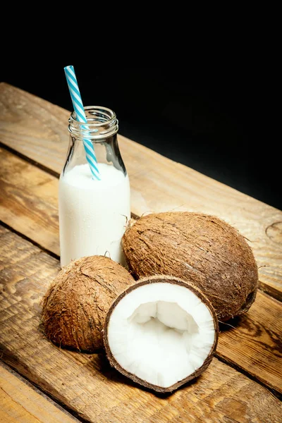 Noci di cocco e bottiglia di latte su un tavolo di legno su sfondo nero — Foto Stock