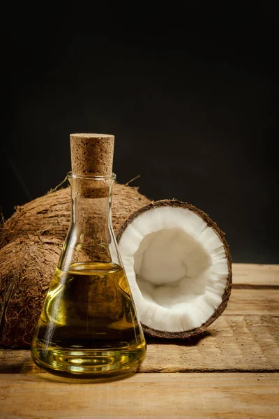 Noci di cocco e una bottiglia di olio su un tavolo di legno su sfondo nero — Foto Stock