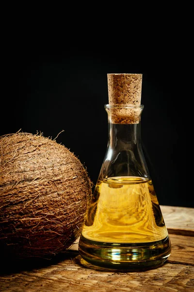 Noci di cocco e una bottiglia di olio su un tavolo di legno su sfondo nero — Foto Stock