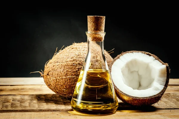 Noci di cocco e una bottiglia di olio su un tavolo di legno su sfondo nero — Foto Stock