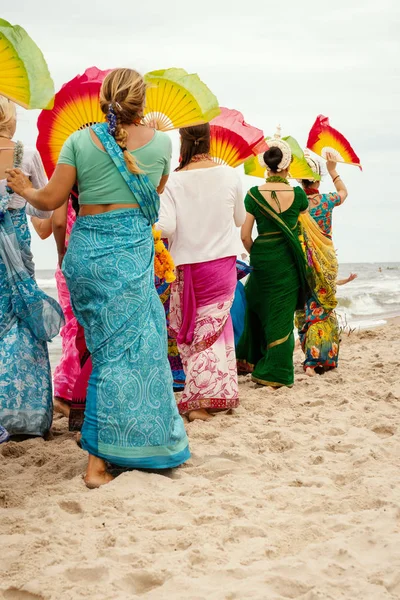 Lebre krishna mulheres em vestidos coloridos estão andando na praia — Fotografia de Stock