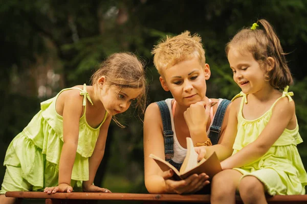 Mutter und zwei entzückende Töchter lesen im Sommerwald ein Buch — Stockfoto