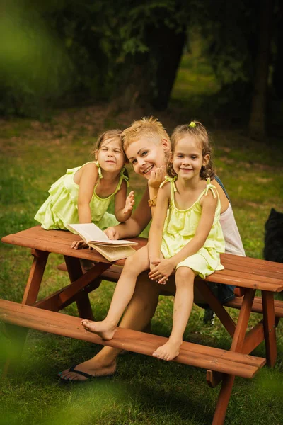 ママと二人の愛らしい娘は夏の森でピクニック テーブルのポーズ — ストック写真