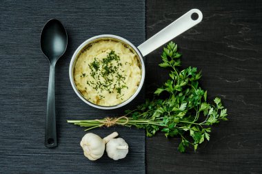 lezzetli ve kremalı taze patates püresi siyah bir tabloda gümüş bir tencerede maydanoz serpilir