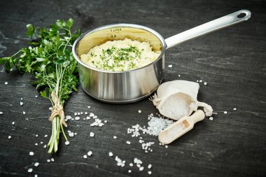 lezzetli ve kremalı taze patates püresi siyah bir tabloda gümüş bir tencerede maydanoz serpilir