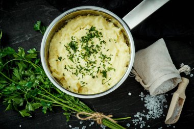 lezzetli ve kremalı taze patates püresi siyah bir tabloda gümüş bir tencerede maydanoz serpilir