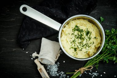 lezzetli ve kremalı taze patates püresi siyah bir tabloda gümüş bir tencerede maydanoz serpilir