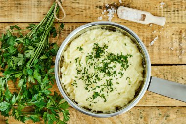 lezzetli ve kremalı taze patates püresi ahşap bir masa üzerinde gümüş bir tencerede maydanoz serpilir