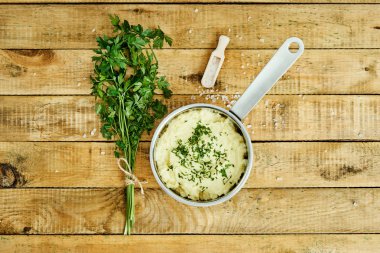 lezzetli ve kremalı taze patates püresi ahşap bir masa üzerinde gümüş bir tencerede maydanoz serpilir