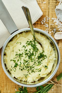 lezzetli ve kremalı taze patates püresi ahşap bir masa üzerinde gümüş bir tencerede maydanoz serpilir