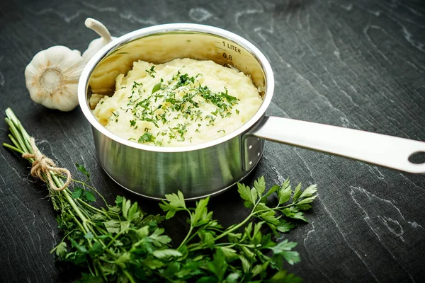 lezzetli ve kremalı taze patates püresi siyah bir tabloda gümüş bir tencerede maydanoz serpilir