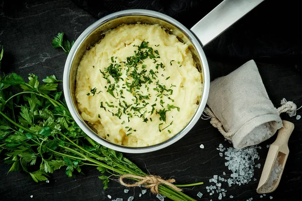 lezzetli ve kremalı taze patates püresi siyah bir tabloda gümüş bir tencerede maydanoz serpilir