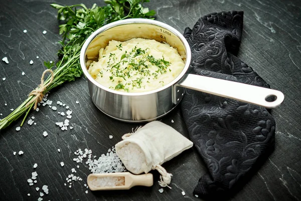 lezzetli ve kremalı taze patates püresi siyah bir tabloda gümüş bir tencerede maydanoz serpilir