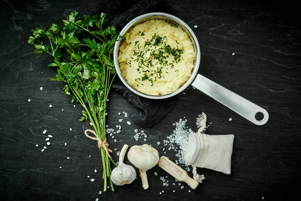 lezzetli ve kremalı taze patates püresi siyah bir tabloda gümüş bir tencerede maydanoz serpilir