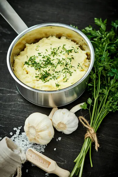 lezzetli ve kremalı taze patates püresi siyah bir tabloda gümüş bir tencerede maydanoz serpilir