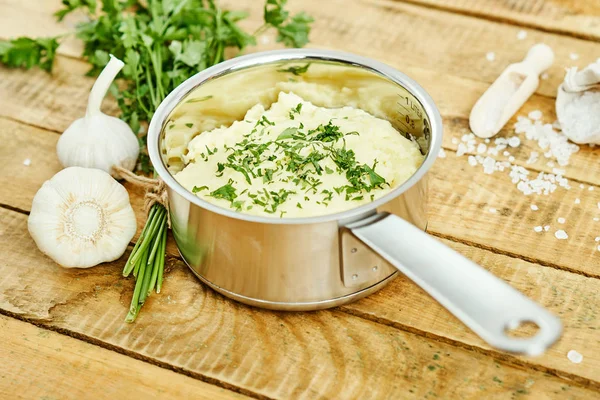 lezzetli ve kremalı taze patates püresi ahşap bir masa üzerinde gümüş bir tencerede maydanoz serpilir