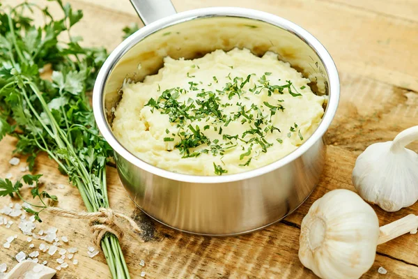 lezzetli ve kremalı taze patates püresi ahşap bir masa üzerinde gümüş bir tencerede maydanoz serpilir