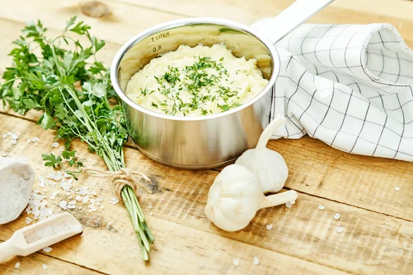 lezzetli ve kremalı taze patates püresi ahşap bir masa üzerinde gümüş bir tencerede maydanoz serpilir