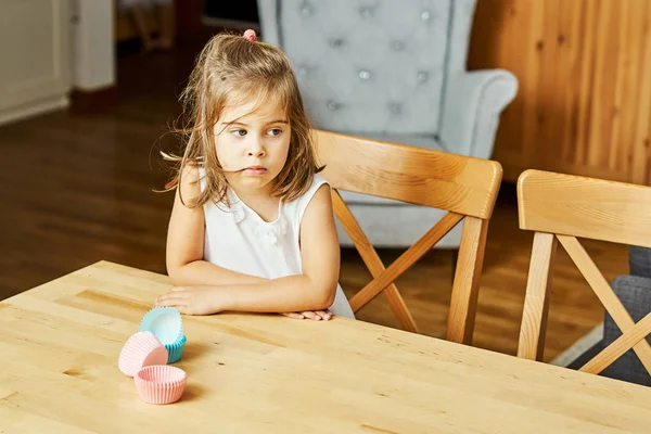 Pequena menina bonita em vestido branco sentado triste na cozinha — Fotografia de Stock