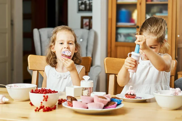 Due belle sorelle in abiti bianchi decorano e mangiano deliziosi cupcake — Foto Stock