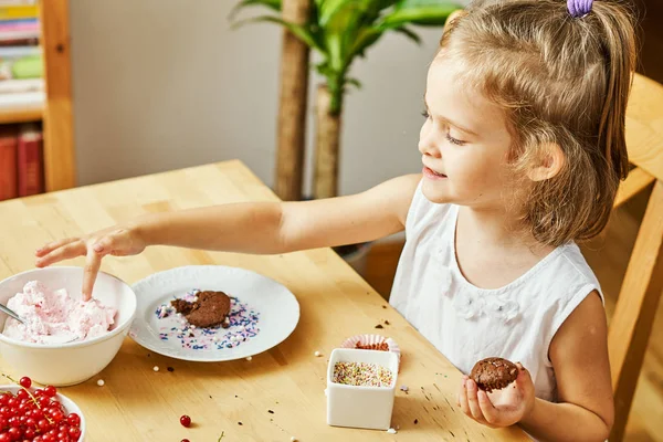 Menina em um vestido branco decora e come um delicioso cupcakes — Fotografia de Stock