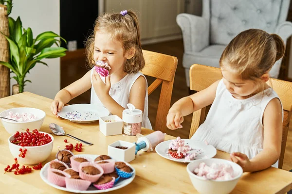 Iki güzel kız kardeş beyaz elbise süslemeleri ve lezzetli kek yemek — Stok fotoğraf