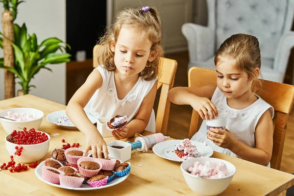 Due belle sorelle in abiti bianchi decorano e mangiano deliziosi cupcake — Foto Stock