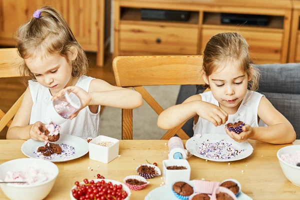 Duas belas irmãs em vestidos brancos decorar e comer deliciosos cupcakes — Fotografia de Stock