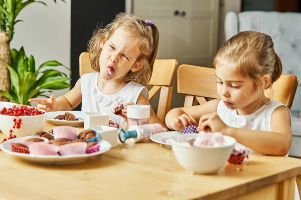 Iki güzel kız kardeş beyaz elbise süslemeleri ve lezzetli kek yemek — Stok fotoğraf