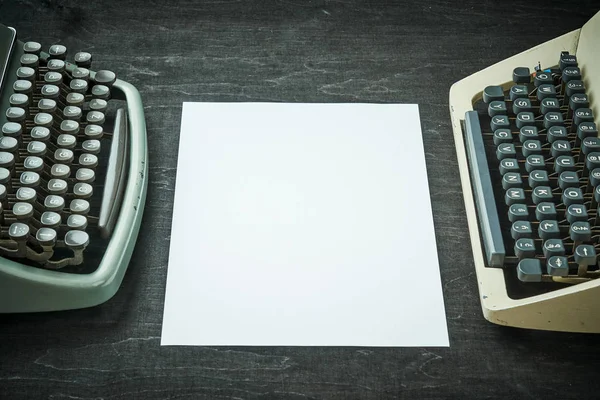 Duas máquinas de escrever velhas e um pedaço de papel em uma mesa preta — Fotografia de Stock