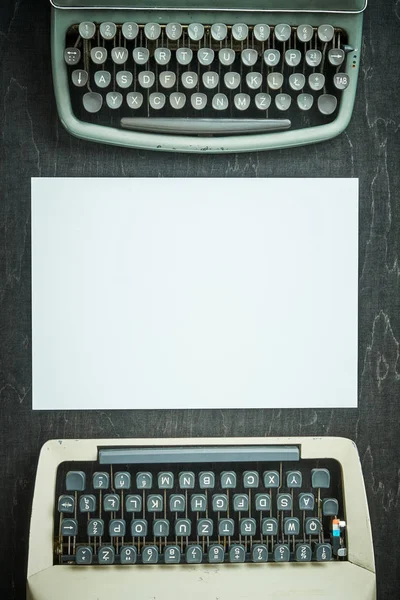 Duas máquinas de escrever velhas e um pedaço de papel em uma mesa preta — Fotografia de Stock