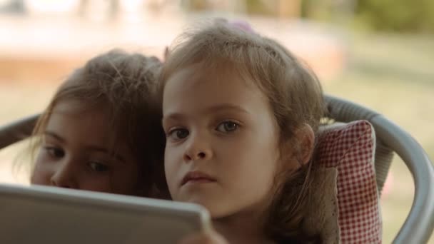 Irmãs bonitos segurar um tablet e assistir a um desenho animado sobre ele — Vídeo de Stock